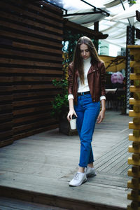 Full length of young woman holding disposable cup at cafe