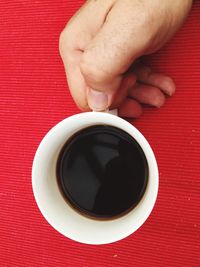 Cropped hand holding black coffee on table