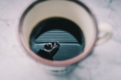 Cropped hand of person reflecting in coffee cup