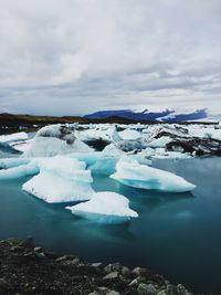 Icebergs in frozen lake against cloudy sky