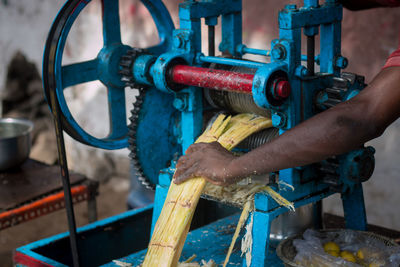 Cropped image of vendor holding sugar cane in machinery