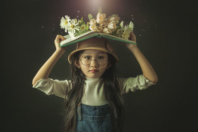 Portrait of cute girl holding flower against black background