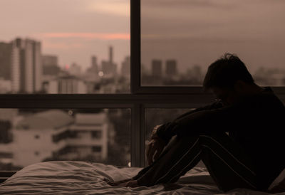 The man sitting on bed with city view from bedroom. stay home, depression and loneliness concept.