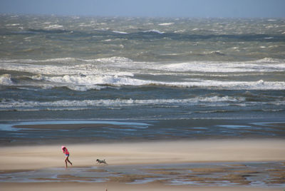 Full length of girl running with dog on beach by sea against sky