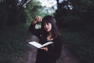 Young woman holding book while standing on tree