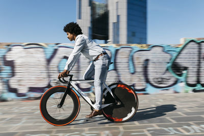 Mid adult man riding bicycle in front of a graffiti wall