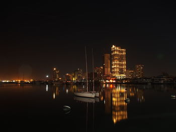 Illuminated buildings by river against sky at night