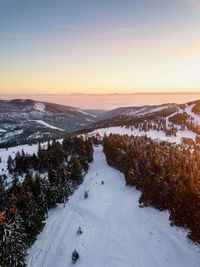 Aerial view of snow covered landscape against sky during sunset