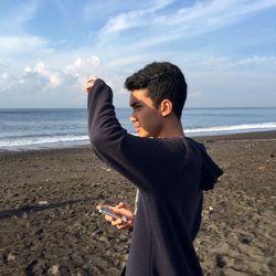 Man shielding eyes while standing on shore at beach during sunny day