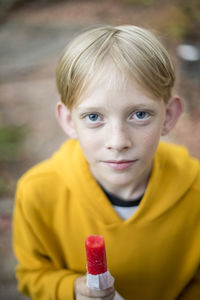 Portrait of teenage boy with blond hair eating red popsicle