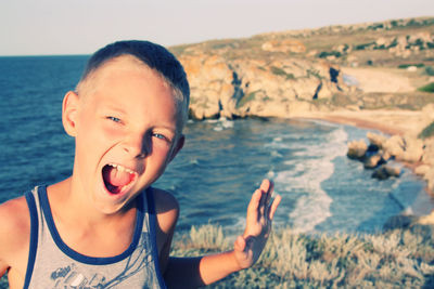 Portrait of boy screaming while standing against sea