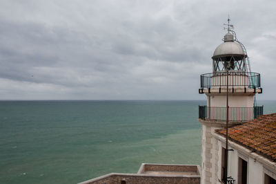 Lighthouse on calm sea against cloudy sky