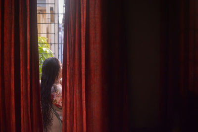 Rear view of woman looking through window at home