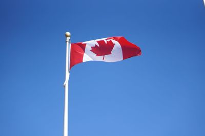 Low angle view of canadian flag against clear blue sky