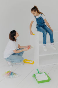Smiling mother and daughter painting wall at home