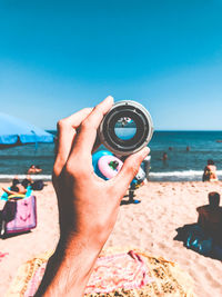 Close-up of hand holding lens at beach against clear sky