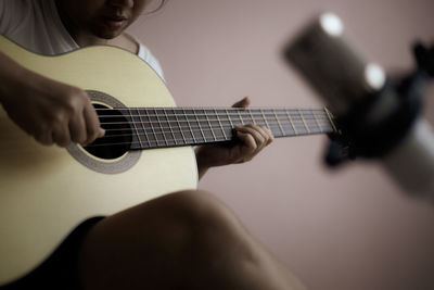 Midsection of woman playing guitar at home