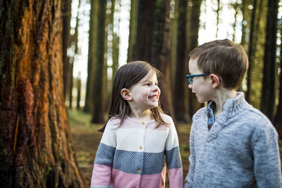 Siblings standing by tree in forest