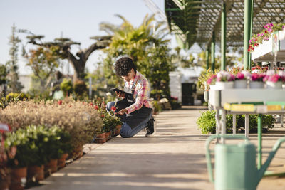 Florist with tablet pc kneeling near plants at nursery
