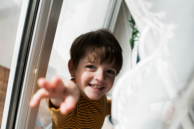 Portrait of smiling boy reaching while standing at home