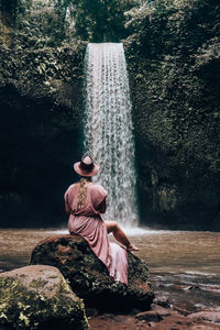 Man sitting on rock by waterfall