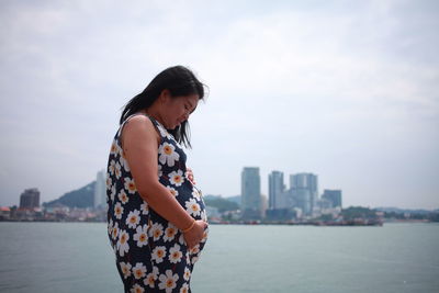 Woman looking at sea by cityscape against sky