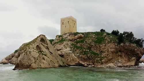 Lighthouse in sea against cloudy sky