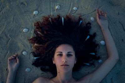 Close-up portrait of woman lying with seashells at beach