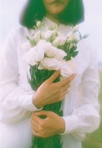 Midsection of woman holding bouquet against white wall