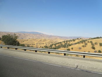 Road leading towards mountains against clear blue sky