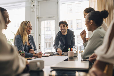 Smiling young entrepreneur discussing business strategy with male and female coworkers in meeting room at office