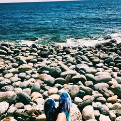 Low section of woman resting on pebbles at beach