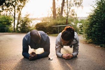 Male and female athletes doing plank exercise on road at park during sunset