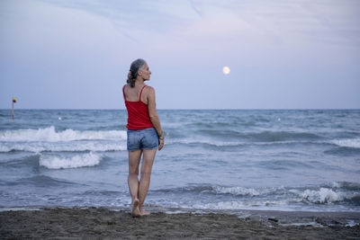 Woman standing at beach with moon over horizon