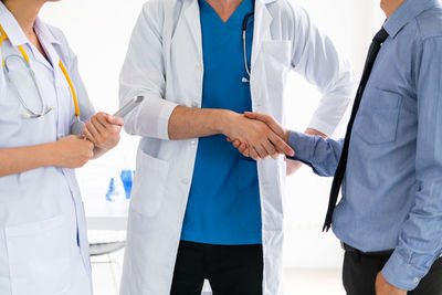 Midsection of doctors shaking hands at clinic