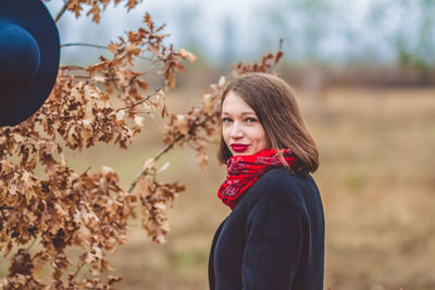 Portrait of smiling woman wearing warm clothing standing by dry plant