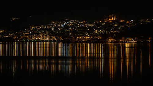 Illuminated buildings by river against sky at night