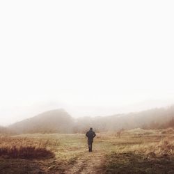 Rear view of man walking on field against clear sky during foggy weather