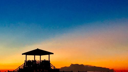 Silhouette lifeguard hut against sky during sunset