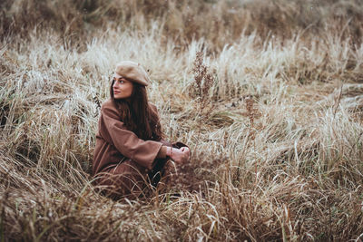 Young woman looking away while sitting on dry grass