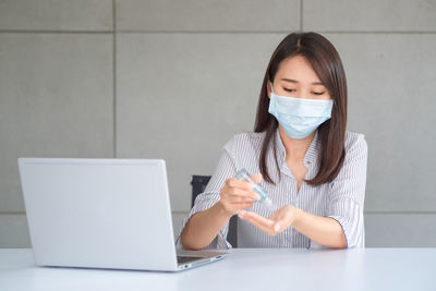 Young woman using sanitizer while sitting on table