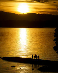 Silhouette people on lake against sky during sunset