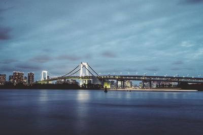 Rainbow bridge over bay of water against sky at dusk