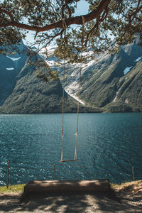 View of empty swing by sea against mountains