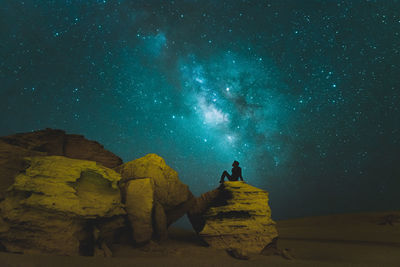 Woman standing by rock formation against sky at night