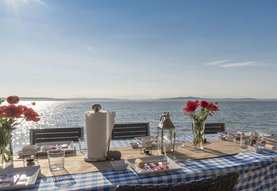 Arranged dining table at beach against blue sky during sunny day