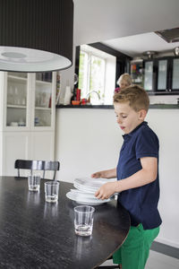 Boy arranging plates on dining table at home