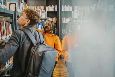 Young friends searching book together in library at university