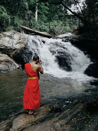 Monk photographing waterfall in forest