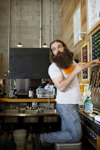 Man with beard standing by beer caps at brewery